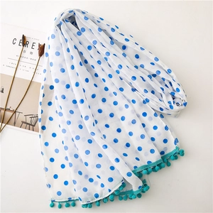Lightweight white scarf with blue polka dots and teal pom-pom trim in a flat lay view