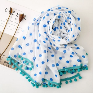 White chiffon scarf with blue polka dots and cyan pom-pom fringe on a styled desk