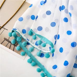 Close-up of translucent white scarf with blue polka dots and green pom-pom trim detail
