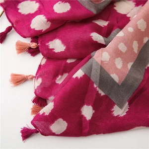 Détail macro d'une écharpe magenta foncé avec tissage à chevrons et glands roses