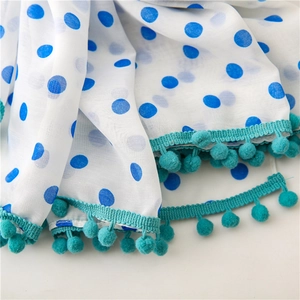 White scarf featuring blue polka dots and green pom-pom trim edge detail