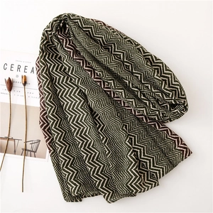 Close-up of a chevron pattern knit scarf in dark green and cream with lifestyle props