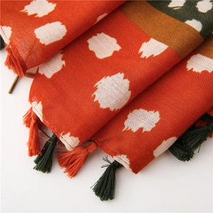 Gros plan sur une écharpe en tissage chevron avec pompons et motifs abstraits orange