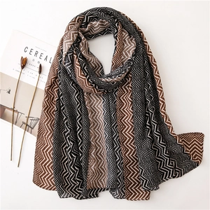 Long chevron pattern scarf in brown and beige tones laid flat with artistic props