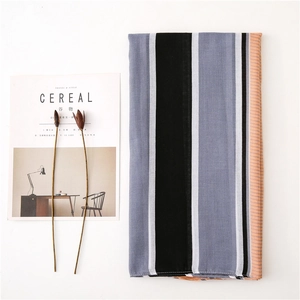 Flat lay of a striped cotton linen scarf with black and pink accents next to a magazine