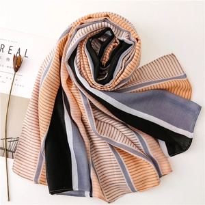 Flat lay of a striped chiffon scarf with orange, black, and blue patterns on white table