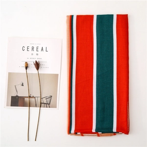 Lifestyle shot of red green and white striped scarf next to a minimal magazine and dried flowers