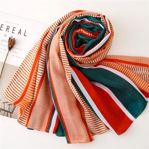 Flat lay of a striped silk scarf in orange and green tones with decorative magazine