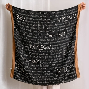 Detail of soft black scarf featuring white cursive text print and caramel brown hem