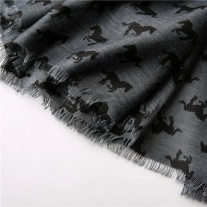 Detail of grey knitted scarf featuring black horse patterns and delicate fringe edges