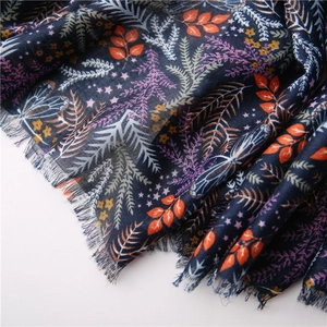 Dettaglio di sciarpa blu scuro con stampe botaniche e bordi a frange fini