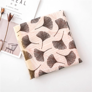 Detail of soft scarf featuring brown ginkgo leaf patterns on light beige fabric