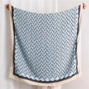 Detail view of cotton linen scarf with floral print and black wavy borders held by hand