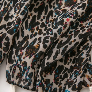 Détail d'une écharpe léopard colorée avec texture en coton lin et pompons blancs