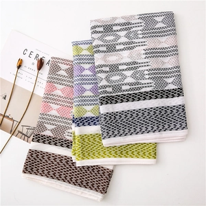 Detail showing folded cotton scarves with geometric weave and fringed edges on white surface