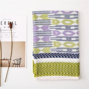 Detail of cotton linen scarf with geometric chain patterns and tassels on white surface