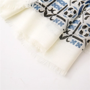 Macro detail of beige cotton linen scarf featuring blue paisley print and tassel edges
