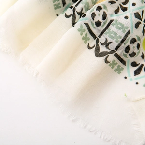 Detailed macro view of beige cotton linen scarf with green floral patterns and fringed edges