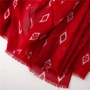 Detail of red scarf with white ikat diamond patterns and raw fringe edges