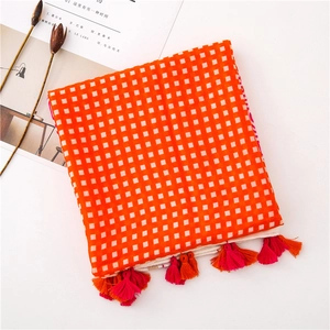 Flat lay detail of orange plaid scarf with vibrant tassels and linen fabric texture