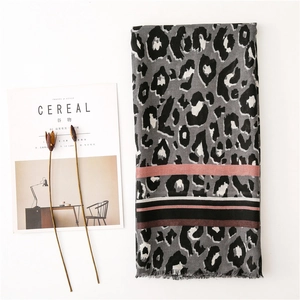 Detailed flat lay of leopard print scarf with pink stripes and fringe edges next to magazine