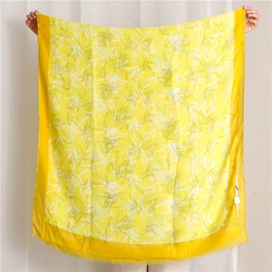 Détail d'une écharpe florale jaune avec motifs de feuilles blanches et bords à franges