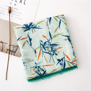 Détail d'une écharpe en coton et lin cyan clair avec imprimés feuilles et bords à franges