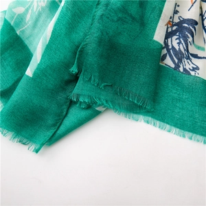 Détail du motif floral vert et des bordures à franges de l'écharpe en coton