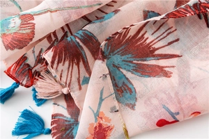 Detail of floral printed shawl with light blue and pink fringe tassels on soft fabric