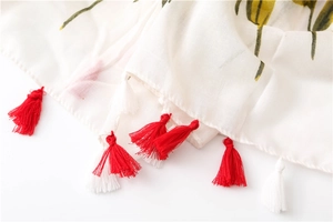 Detailed macro view of red and white tassels and green plant print on cotton linen scarf