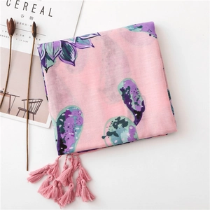 Détail d'une écharpe en coton rose à motif floral avec pompons et texture légère