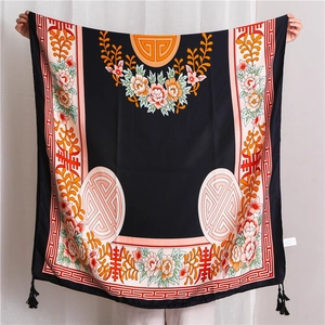 Detailed view of black silk-like scarf with floral patterns and fringe edges