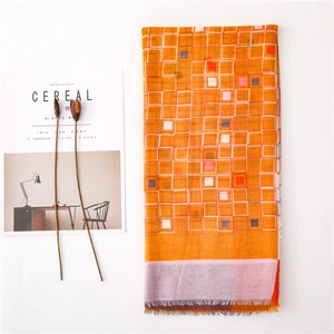 Détail d'une écharpe à carreaux orange avec glands et franges sur fond blanc chaleureux