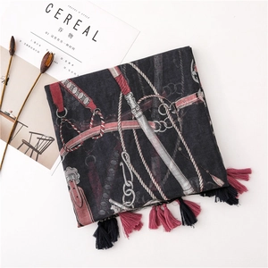 Detailed flat lay of a grey scarf with horse harness print and tassel trim near a magazine