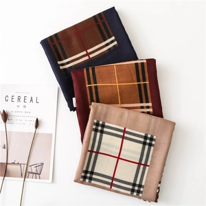 Flat lay of folded plaid scarves in navy, red and apricot with minimalist decor