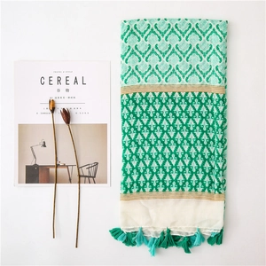 Detail of green and white patterned cotton linen scarf with turquoise tassel fringe
