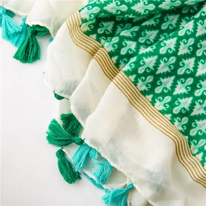 Detail of white cotton linen scarf with green floral prints and turquoise tassels