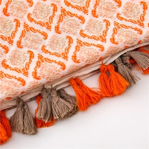 Detail of cream linen scarf featuring orange geometric patterns and colorful tassels