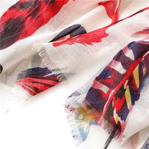 Detailed close-up of colorful feather print on white cotton-linen shawl with fringe