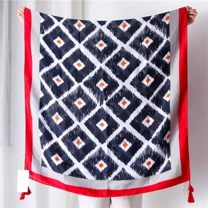 Détail de l'écharpe géométrique rouge et noire avec glands aux coins et texture en coton doux