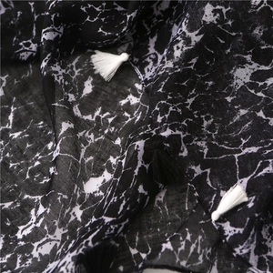 Macro detail of marble pattern fabric scarf with decorative black and white tassels