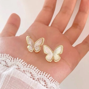 Detail of gold butterfly stud earrings with white shell and zircon held in hand