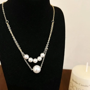 Detail of elegant gold-tone layered necklace with pearls on a black display stand