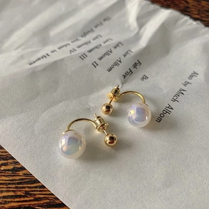 Minimalist C-shaped gold earrings with iridescent mermaid pearls on a vintage paper