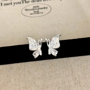 Macro detail of silver butterfly studs with cubic zirconia drop on black velvet