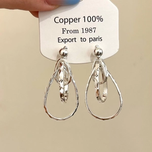 Détail de boucles d'oreilles goutte argentées avec anneaux imbriqués et texture martelée