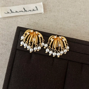 Detailed close-up of golden fountain tassel earrings with white pearls and small zircons