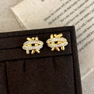 Macro view of gold-tone braided stud earrings with pave-set cubic zirconia on a stand