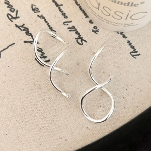 Close-up of silver spiral geometric earrings on artistic fabric with a candle background