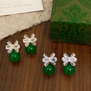 Detailed view of crystal bow earrings with emerald green beads on a vintage wooden surface